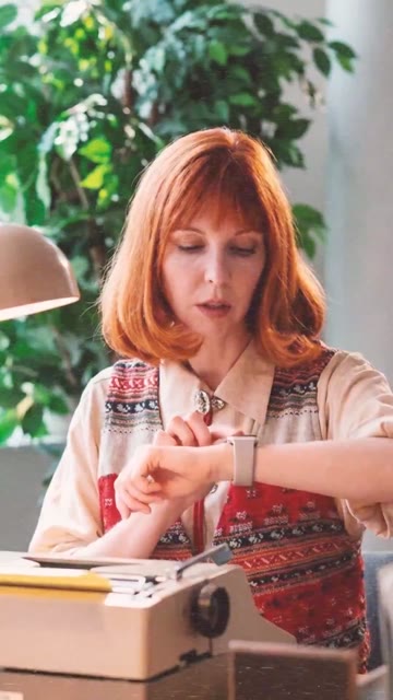 Standbild: Frau am Schreibtisch schaut auf ihre Armbanduhr.